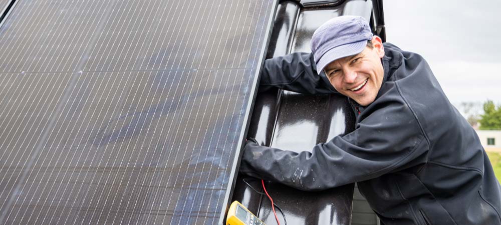 Ein Techniker mit Kappe montiert ein Solarmodul auf dem Dach
